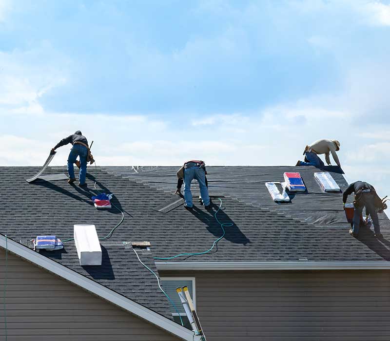 Workers on a residential roof installing new gray shingles